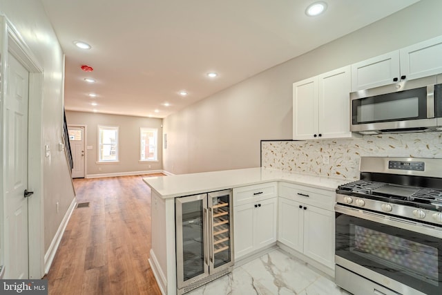 kitchen featuring kitchen peninsula, stainless steel appliances, tasteful backsplash, wine cooler, and white cabinets