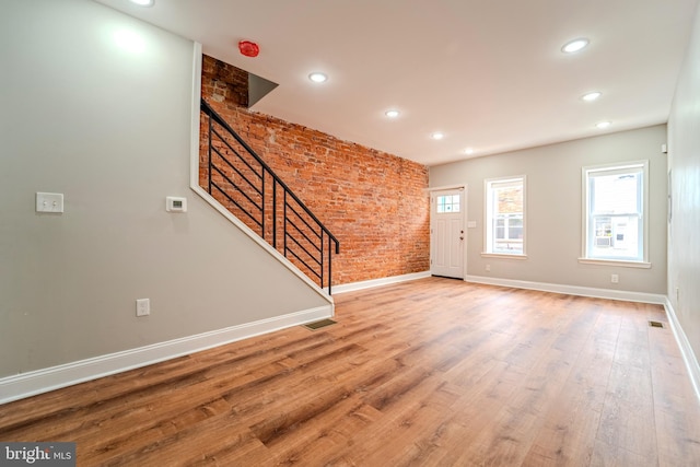 unfurnished living room featuring brick wall and hardwood / wood-style flooring