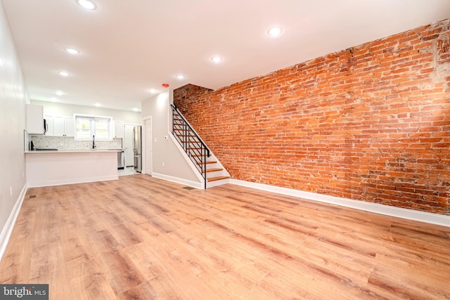 unfurnished living room featuring brick wall and light hardwood / wood-style floors