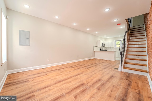 unfurnished living room featuring electric panel and light hardwood / wood-style floors