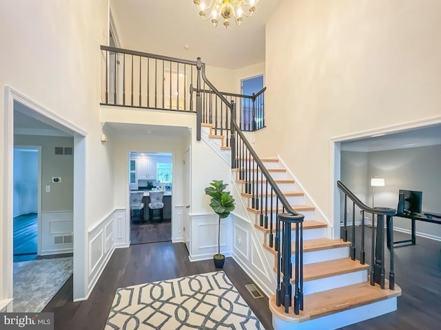 staircase with a towering ceiling, an inviting chandelier, and hardwood / wood-style floors