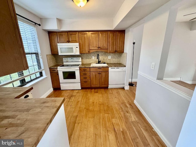 kitchen with tasteful backsplash, sink, white appliances, and light hardwood / wood-style floors