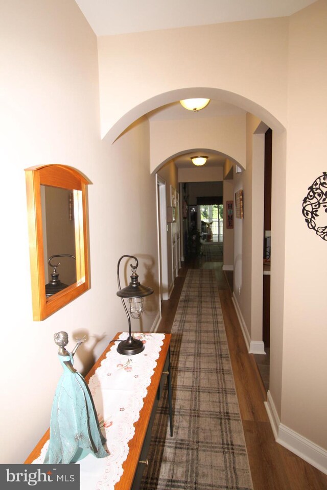 corridor with wood finished floors, baseboards, and arched walkways