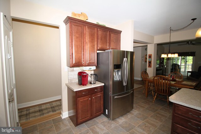 kitchen with backsplash, baseboards, light countertops, an inviting chandelier, and stainless steel fridge