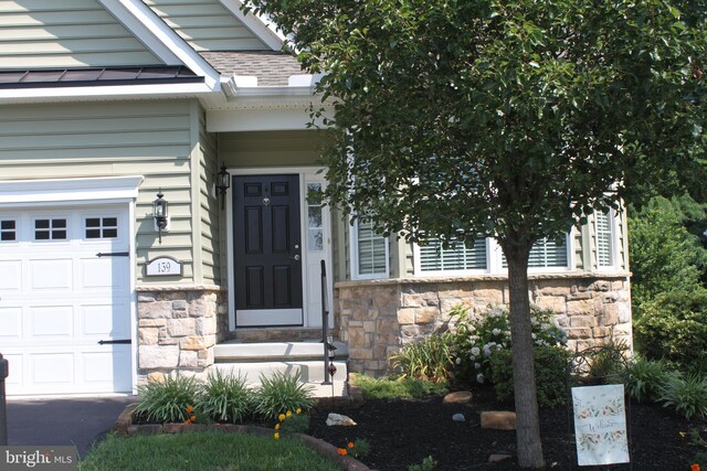 doorway to property with a garage, stone siding, and roof with shingles