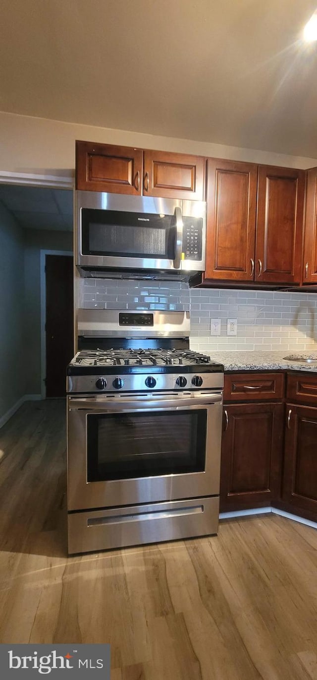 kitchen with appliances with stainless steel finishes, decorative backsplash, light stone counters, and light wood-type flooring