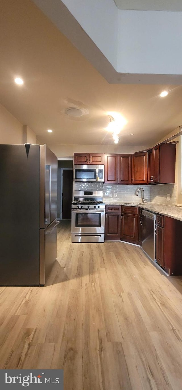 kitchen featuring light stone counters, light wood-type flooring, stainless steel appliances, and backsplash