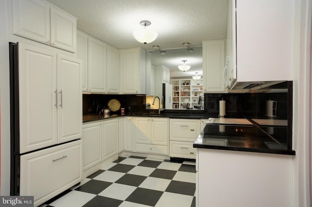 kitchen with tasteful backsplash, sink, white cabinets, fridge, and a textured ceiling