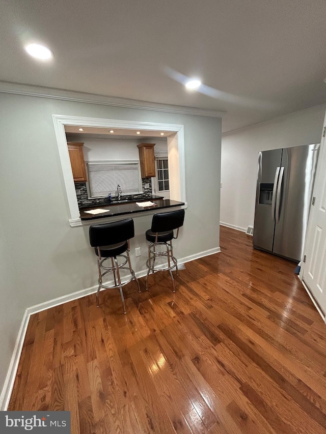 kitchen with stainless steel fridge with ice dispenser, backsplash, a kitchen breakfast bar, kitchen peninsula, and dark wood-type flooring