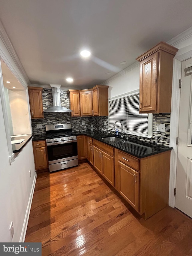 kitchen with wall chimney exhaust hood, sink, light wood-type flooring, ornamental molding, and stainless steel range with gas stovetop