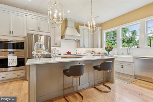 kitchen with custom exhaust hood, light wood-type flooring, a center island, a breakfast bar area, and appliances with stainless steel finishes