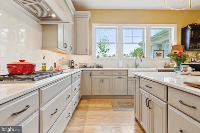 kitchen with stainless steel gas stovetop, sink, decorative backsplash, light wood-type flooring, and custom range hood