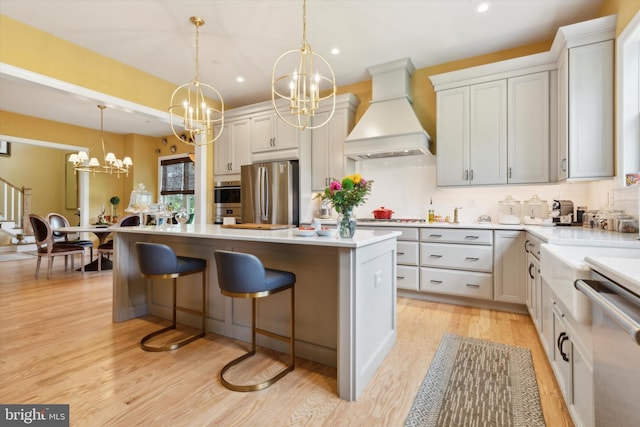 kitchen with white cabinets, appliances with stainless steel finishes, a kitchen island, decorative light fixtures, and premium range hood