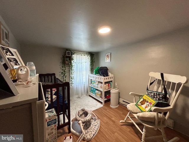 bedroom with hardwood / wood-style floors, a nursery area, and a baseboard heating unit