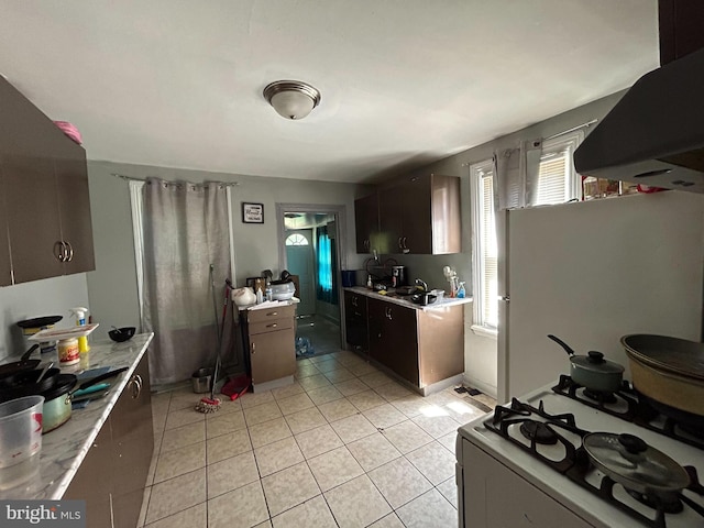 kitchen with white appliances, light tile patterned floors, dark brown cabinets, and exhaust hood