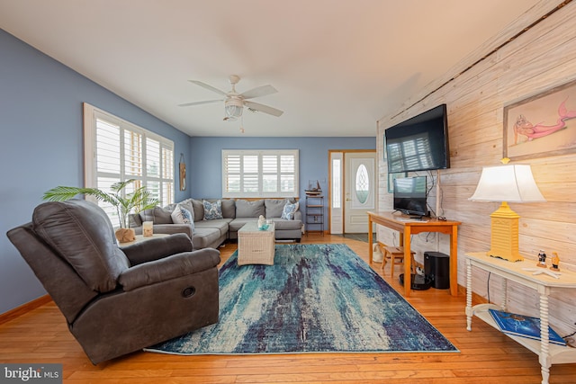 living room featuring ceiling fan, light wood-type flooring, and wood walls