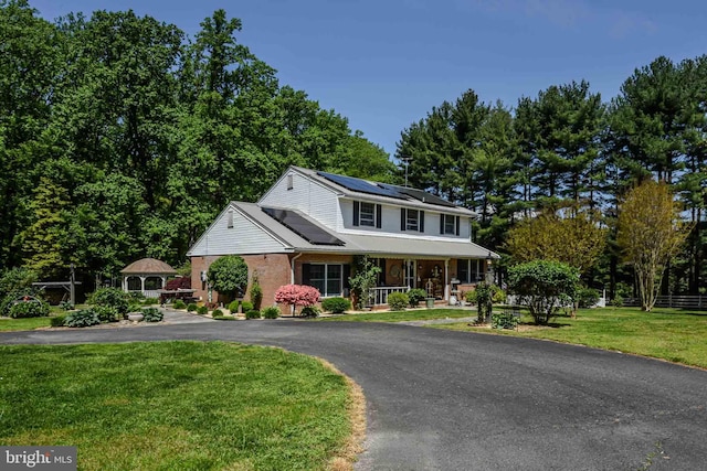 view of front of home featuring a front lawn, solar panels, and a porch