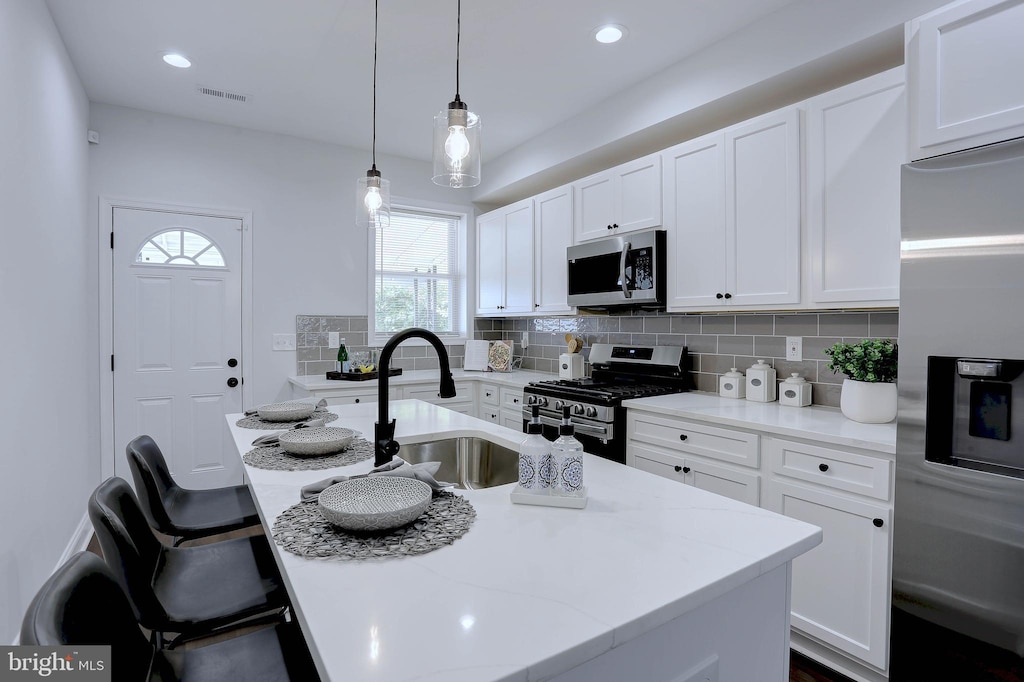 kitchen with appliances with stainless steel finishes, decorative light fixtures, white cabinetry, an island with sink, and sink