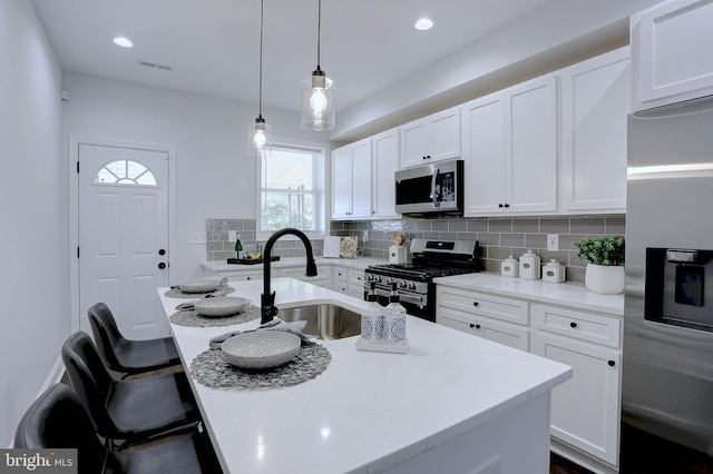 kitchen featuring white cabinetry, an island with sink, appliances with stainless steel finishes, decorative light fixtures, and sink