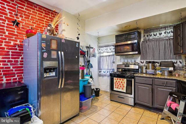 kitchen featuring brick wall, light stone counters, stainless steel appliances, and light tile patterned floors