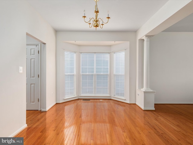 unfurnished dining area featuring a chandelier, decorative columns, and light hardwood / wood-style flooring