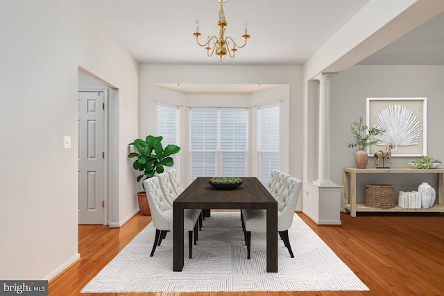 dining area with light hardwood / wood-style floors, decorative columns, and a notable chandelier