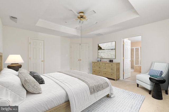 bedroom featuring ceiling fan, connected bathroom, a tray ceiling, light carpet, and a closet