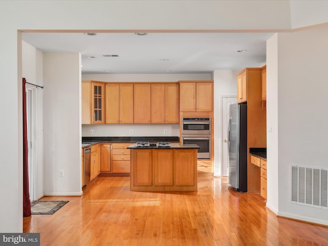 kitchen with dark stone countertops, a kitchen island, light hardwood / wood-style floors, and appliances with stainless steel finishes