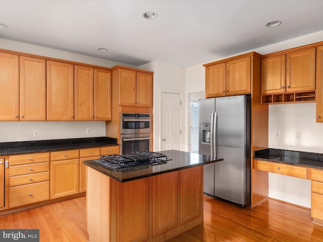 kitchen with built in desk, light wood-type flooring, dark stone counters, a kitchen island, and stainless steel appliances