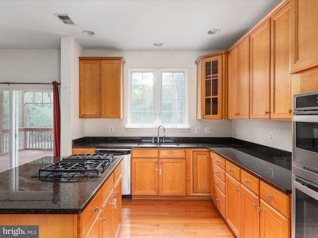 kitchen with appliances with stainless steel finishes, sink, light hardwood / wood-style flooring, and dark stone countertops