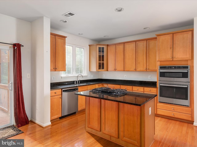 kitchen featuring a kitchen island, sink, dark stone countertops, stainless steel appliances, and light wood-type flooring