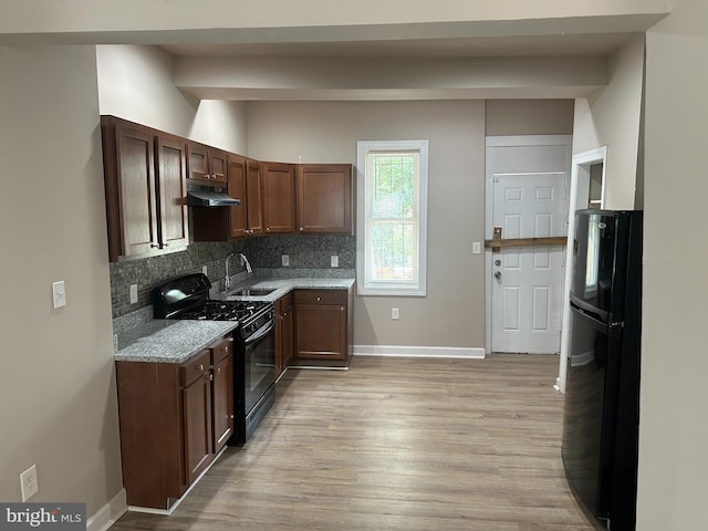 kitchen with backsplash, light stone countertops, black appliances, light hardwood / wood-style flooring, and sink