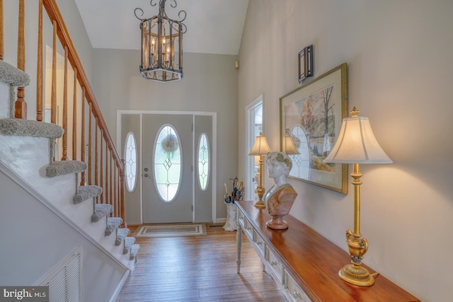 foyer entrance with wood-type flooring, a notable chandelier, and a high ceiling