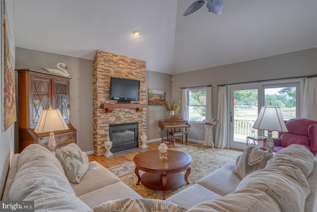 living room with a stone fireplace, light wood-type flooring, ceiling fan, and high vaulted ceiling