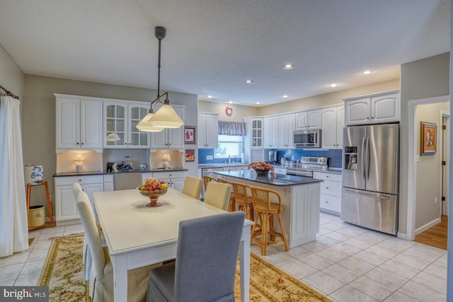 kitchen with light wood-type flooring, white cabinets, a kitchen island, hanging light fixtures, and appliances with stainless steel finishes