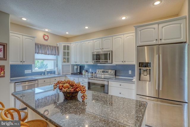 kitchen with a breakfast bar, white cabinets, dark stone counters, stainless steel appliances, and sink