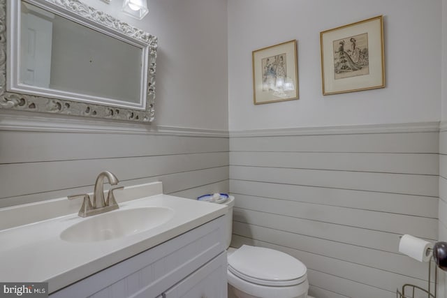 bathroom featuring wood walls, toilet, and vanity