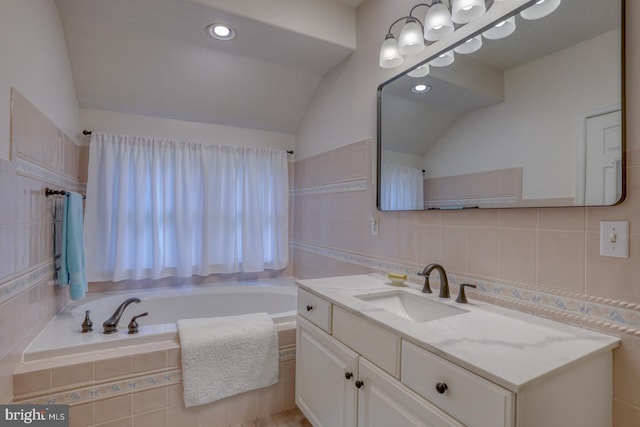 bathroom with a relaxing tiled tub, vanity, tile walls, and vaulted ceiling