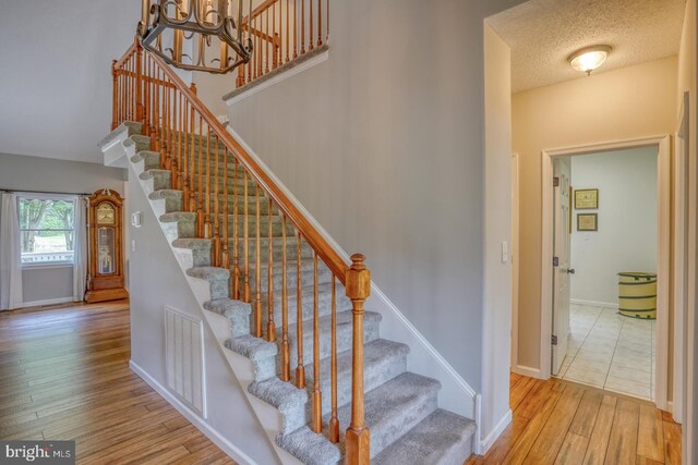 stairs featuring light hardwood / wood-style floors, an inviting chandelier, and a textured ceiling