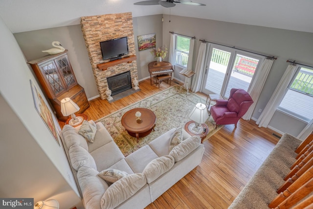 living room with a stone fireplace, lofted ceiling, light hardwood / wood-style flooring, and ceiling fan