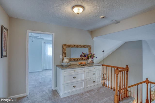 hallway featuring vaulted ceiling, light colored carpet, and a textured ceiling