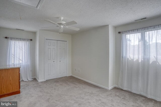 unfurnished bedroom with a closet, a textured ceiling, ceiling fan, and light colored carpet