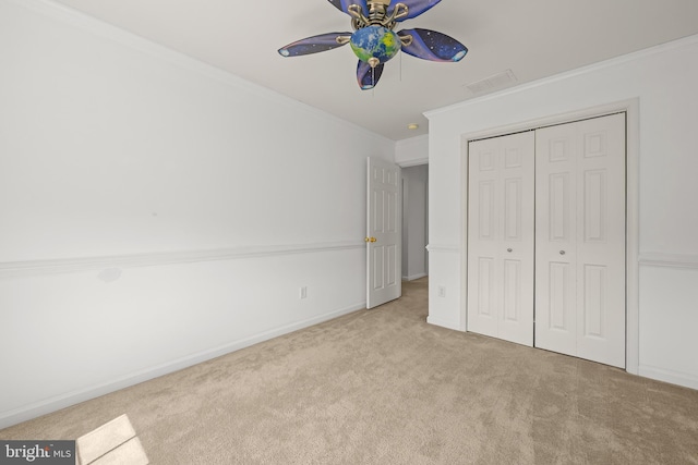 unfurnished bedroom featuring ceiling fan, light colored carpet, a closet, and crown molding