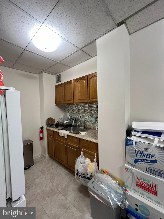 kitchen featuring a drop ceiling, white refrigerator, decorative backsplash, sink, and light stone countertops