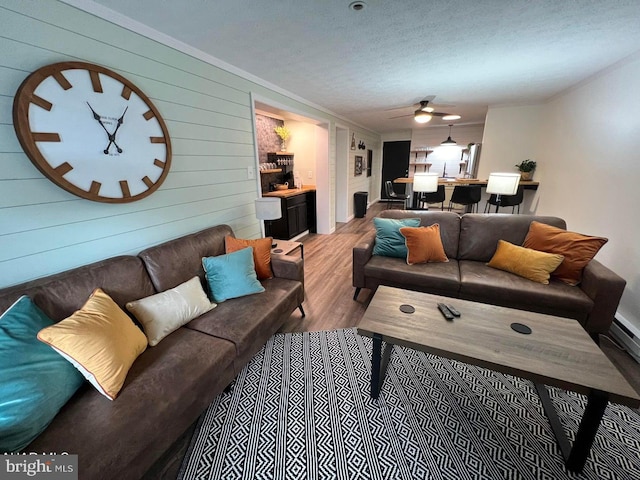 living room featuring ceiling fan, wood walls, light hardwood / wood-style flooring, a textured ceiling, and ornamental molding