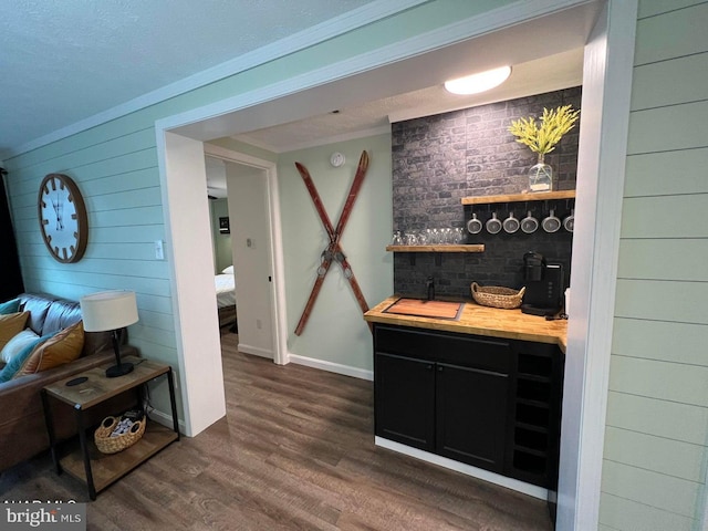 bar with dark wood-type flooring, ornamental molding, wood walls, and wooden counters