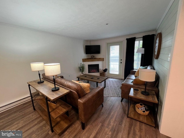 living room featuring a textured ceiling, a baseboard heating unit, dark hardwood / wood-style flooring, a fireplace, and ornamental molding