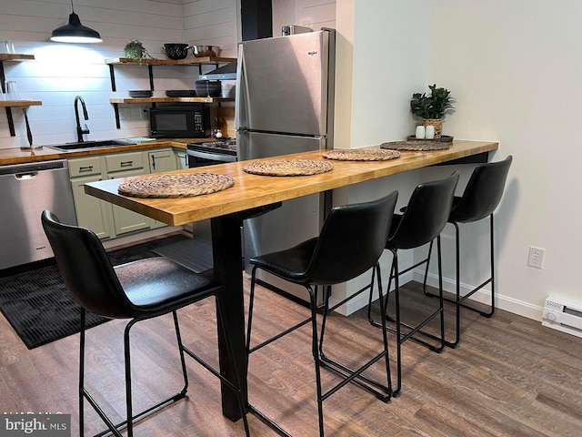 kitchen with butcher block counters, green cabinets, appliances with stainless steel finishes, wood-type flooring, and pendant lighting