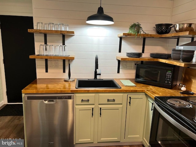 kitchen with wood counters, wooden walls, decorative light fixtures, black appliances, and sink