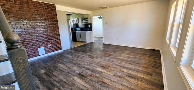 unfurnished living room with brick wall and dark hardwood / wood-style floors